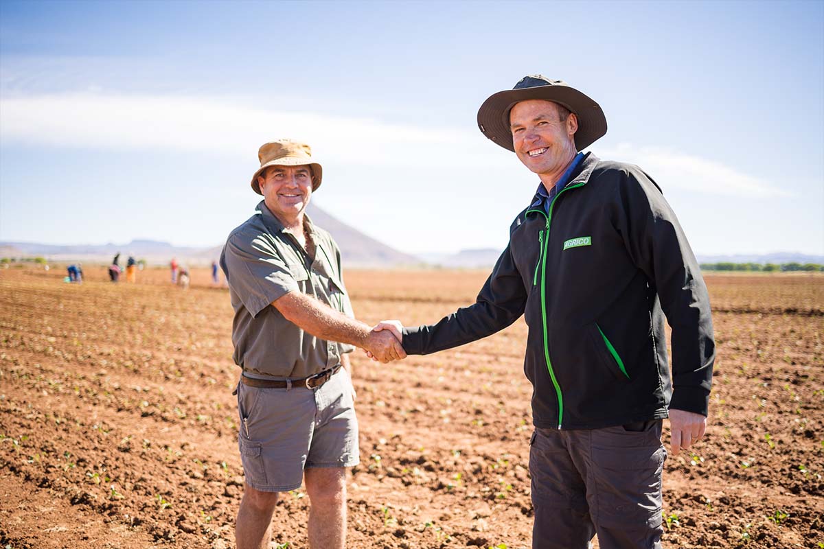 2 men shaking hands and smiling in a field